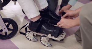 Stroke patient in wheel chair strapping GEMS shoe on. SciTech Now episode 313 YouTube:Wpsu.jpeg