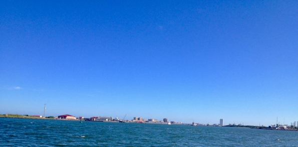 Galveston's bay side as seen from ferry. Buildings left to right: Coast Guard Station, UTMB Medical in center, far right is Sea Wolf Park Pavilion - and at the right edge are a large number of jack up rigs waiting for refurbishing or to be towed out to a job site in the Gulf of Mexico (©All rights reserved, copyrighted, NO permissions granted)