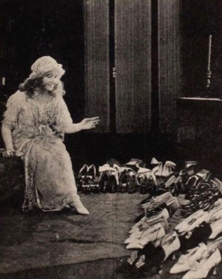Woman surrounded by rows ands rows of shoes. Bessie Barriscale, 1921, Exhibitors Herald, 1921. USPD, artist life, pub.date/Commons.wikimedia.org)
